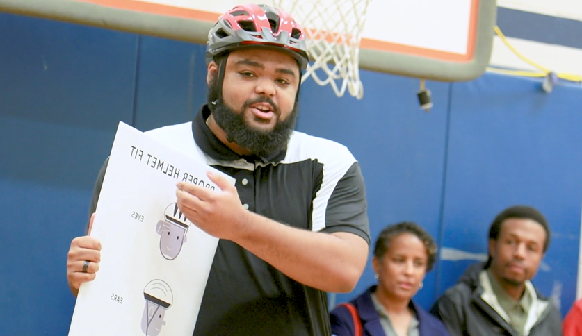 体育老师一边说话一边举着写着“头盔合适”的牌子."